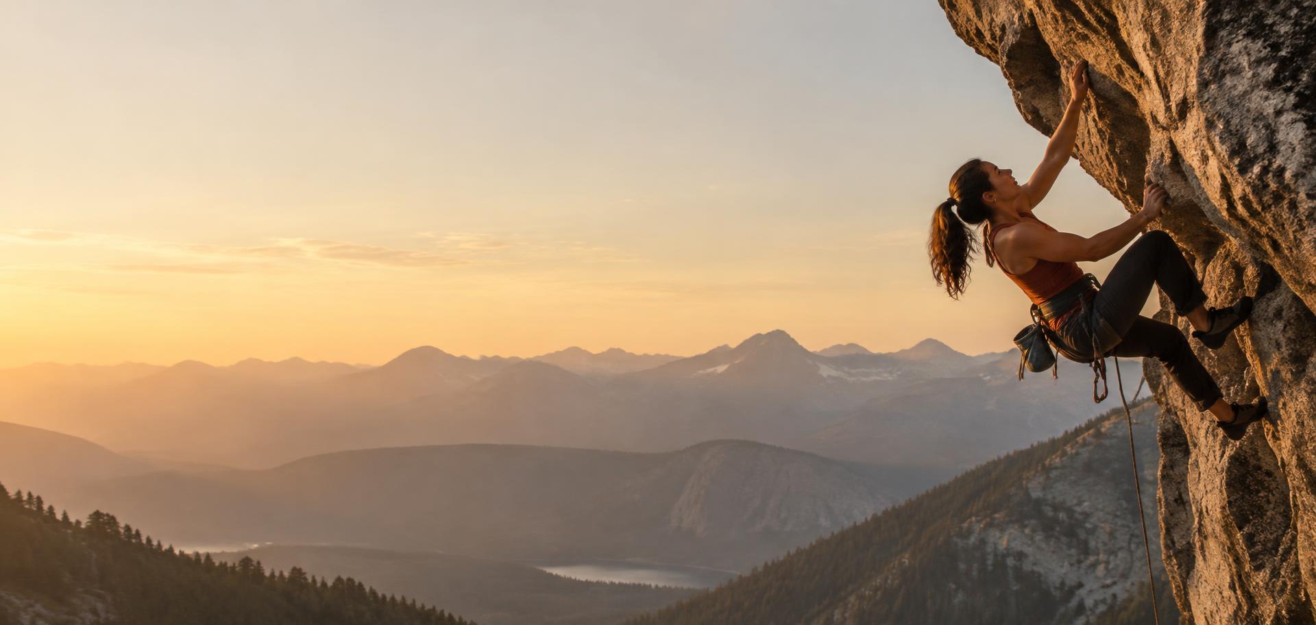 Climber on an overhanging cliff above a mountain valley at sunset